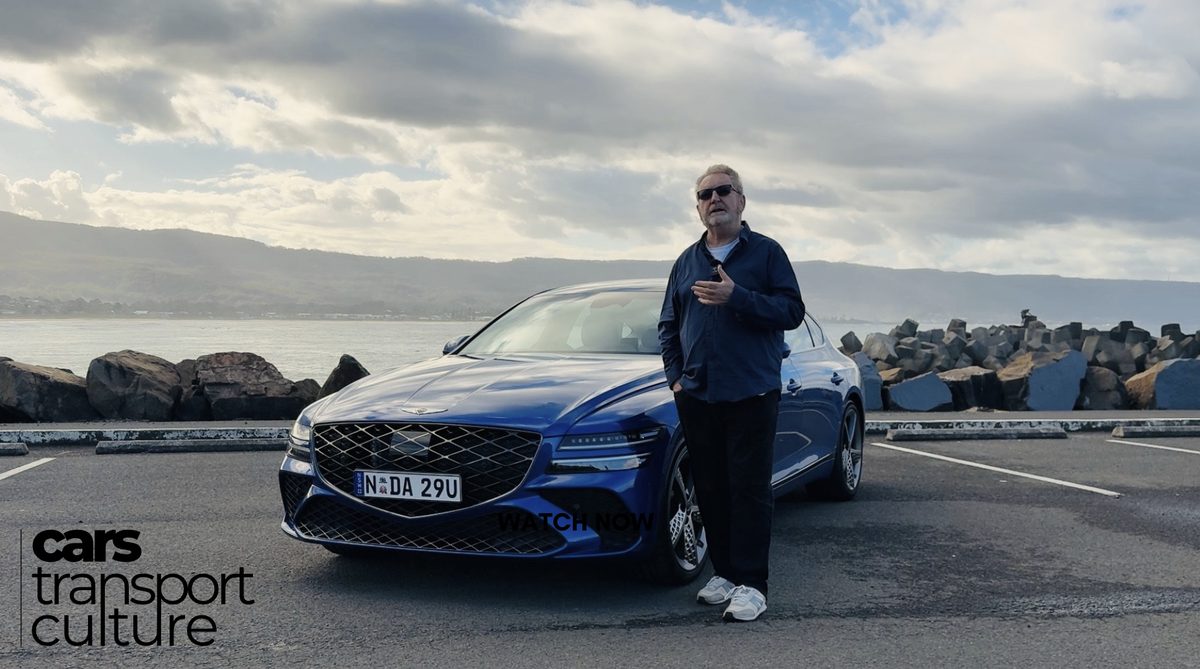 David Brown presenting a road test beside a blue Genesis sedan